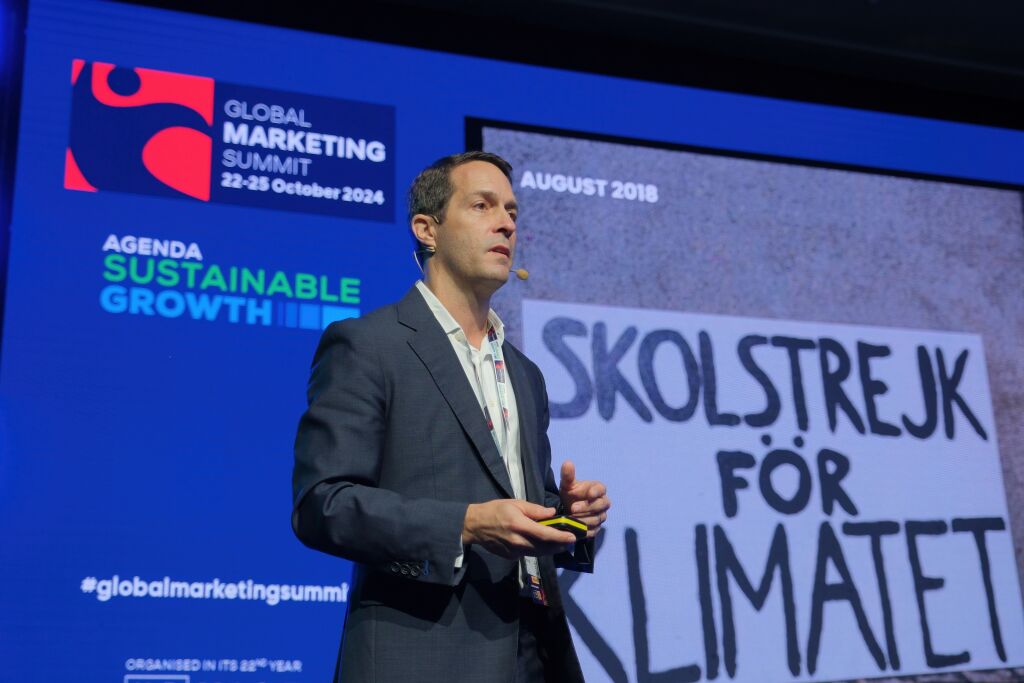 A keynote speaker presents on stage at the Global Marketing Summit 2024, with a blue “Sustainable Growth” agenda backdrop and a large projected slide showing climate strike text in Swedish.